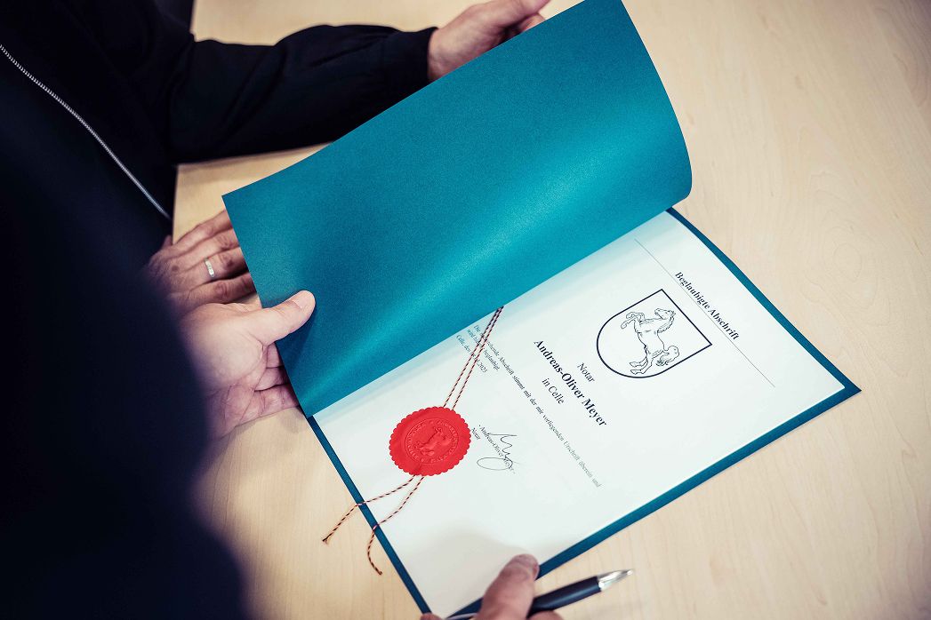 Eine Person hält ein Zertifikat über einem Tisch.